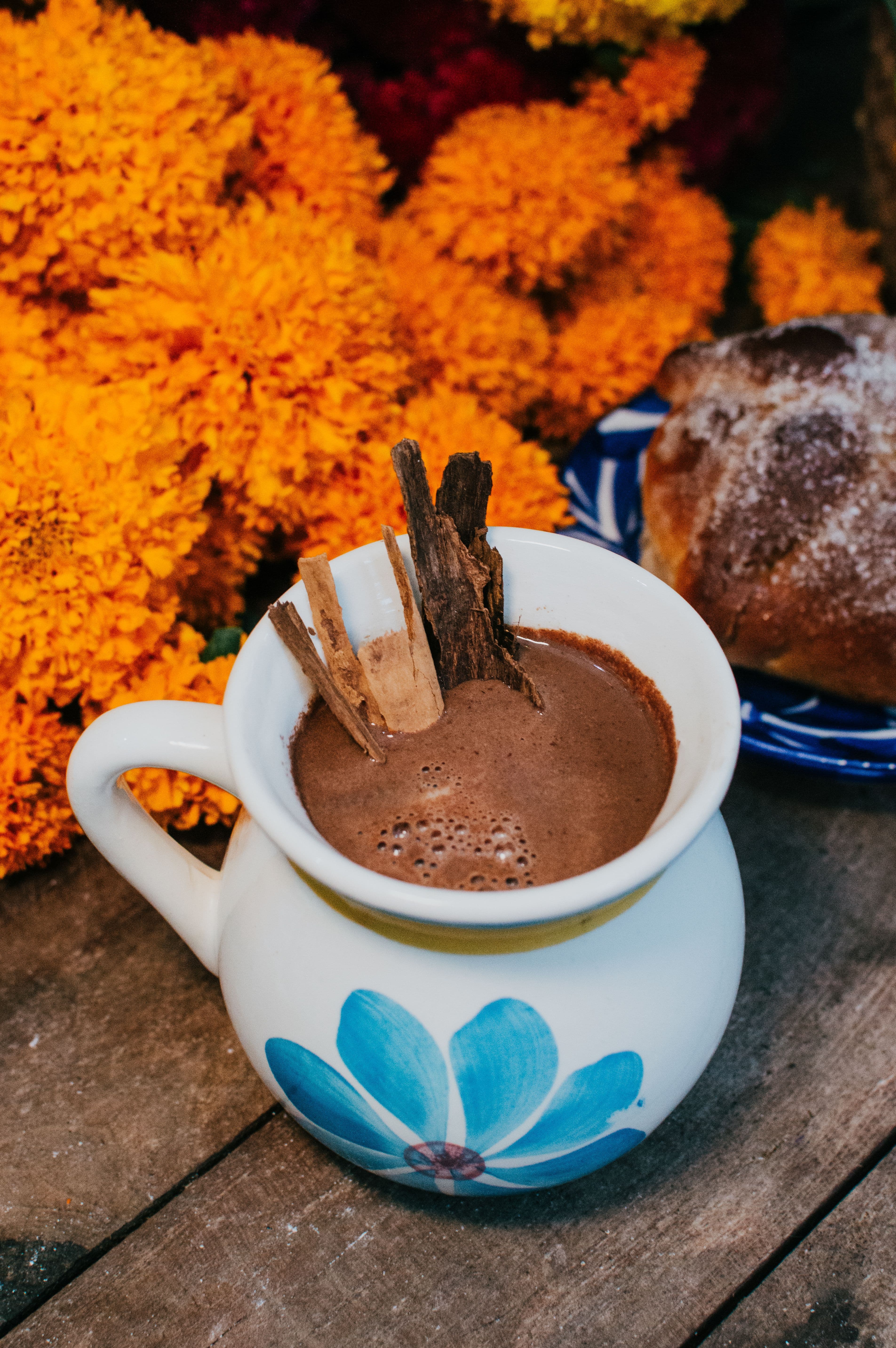 Jarrito de chocolate caliente con canela junto a pan de muerto y cempasúchil